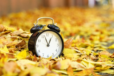 Photo of Autumn time. Alarm clock on fallen leaves, closeup