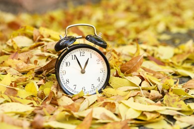 Photo of Autumn time. Alarm clock on fallen leaves, closeup