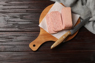 Photo of Tasty canned meat and knife on wooden table, top view. Space for text