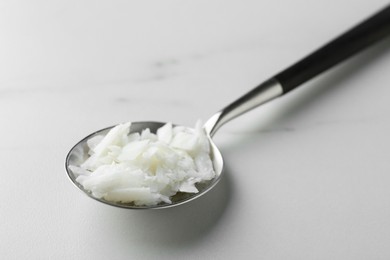 Photo of Soy wax in spoon on white marble table, closeup