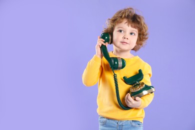 Photo of Cute little boy with old telephone on violet background, space for text