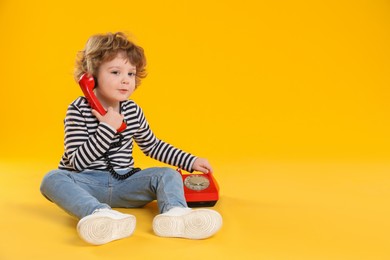 Photo of Cute little boy with telephone on orange background, space for text