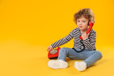 Photo of Cute little boy with telephone on orange background, space for text