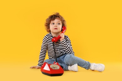 Photo of Cute little boy with telephone on orange background