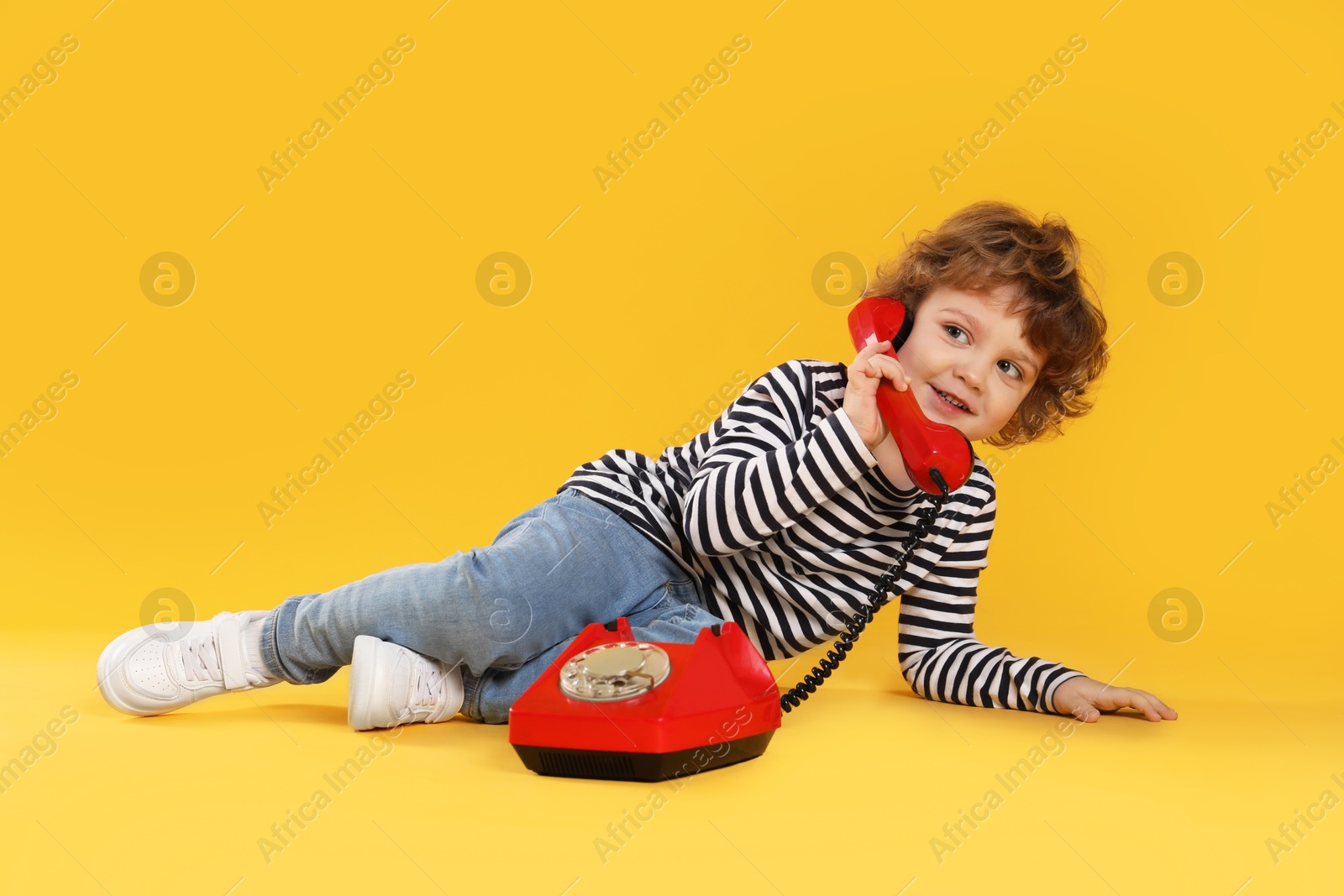 Photo of Cute little boy with telephone on orange background