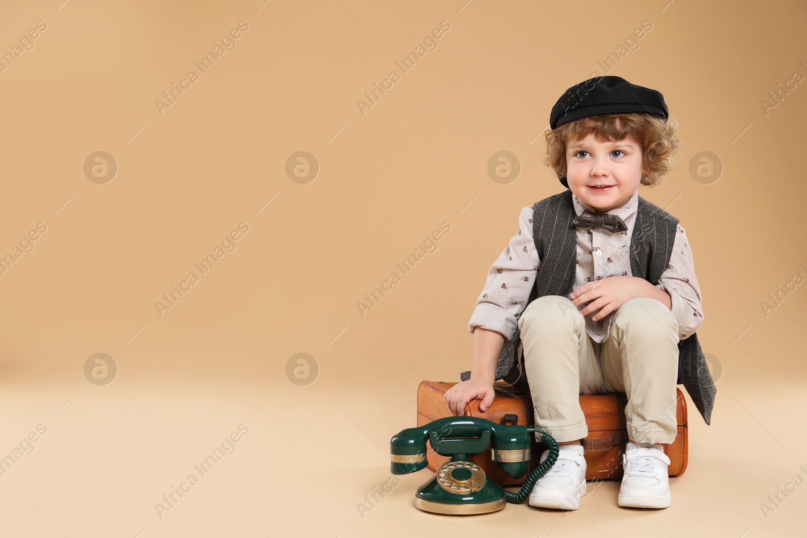 Photo of Cute little boy with old telephone and suitcase on beige background, space for text