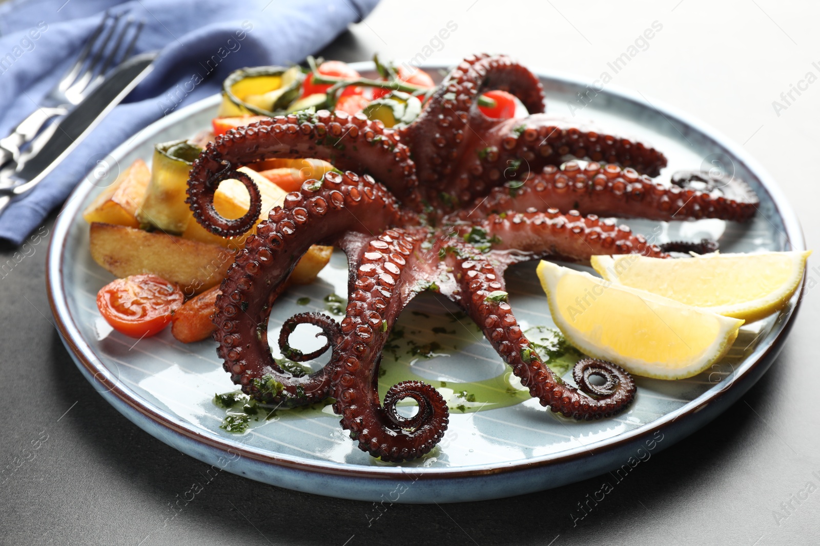 Photo of Fried octopus with herb sauce, lemon and vegetables on grey table, closeup