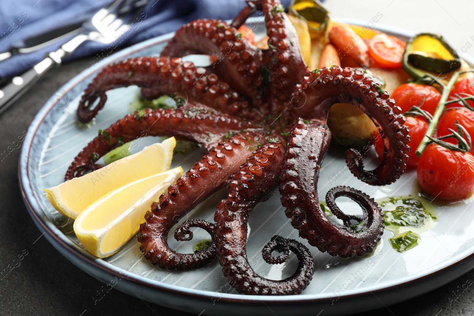 Photo of Fried octopus with herb sauce, lemon and vegetables on grey table, closeup