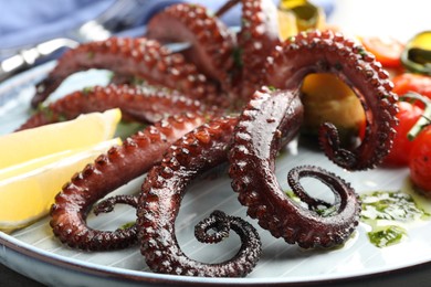 Photo of Fried octopus with herb sauce, lemon and vegetables on table, closeup