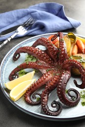 Photo of Fried octopus with herb sauce, lemon and vegetables on grey table, closeup