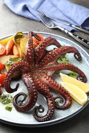 Photo of Fried octopus with herb sauce, lemon and vegetables on grey table, closeup