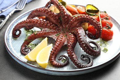 Photo of Fried octopus with herb sauce, lemon and vegetables on grey table, closeup