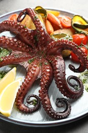 Photo of Fried octopus with herb sauce, lemon and vegetables on grey table, closeup