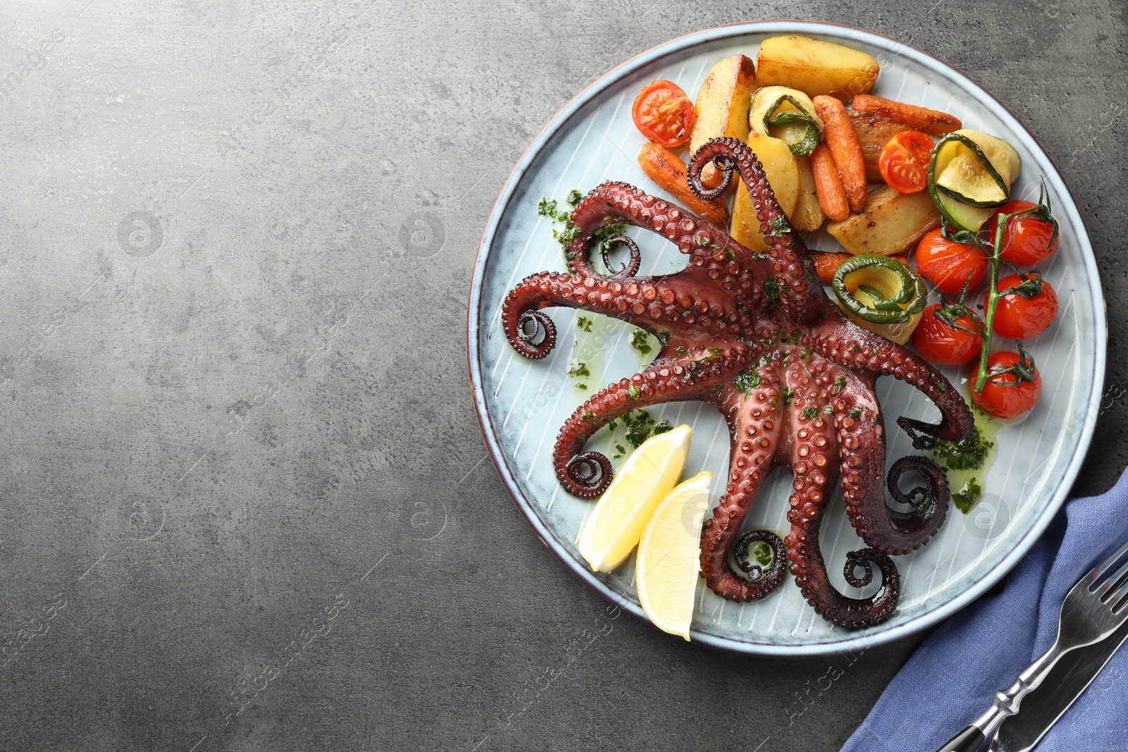 Photo of Fried octopus with herb sauce, lemon and vegetables on grey textured table, top view. Space for text