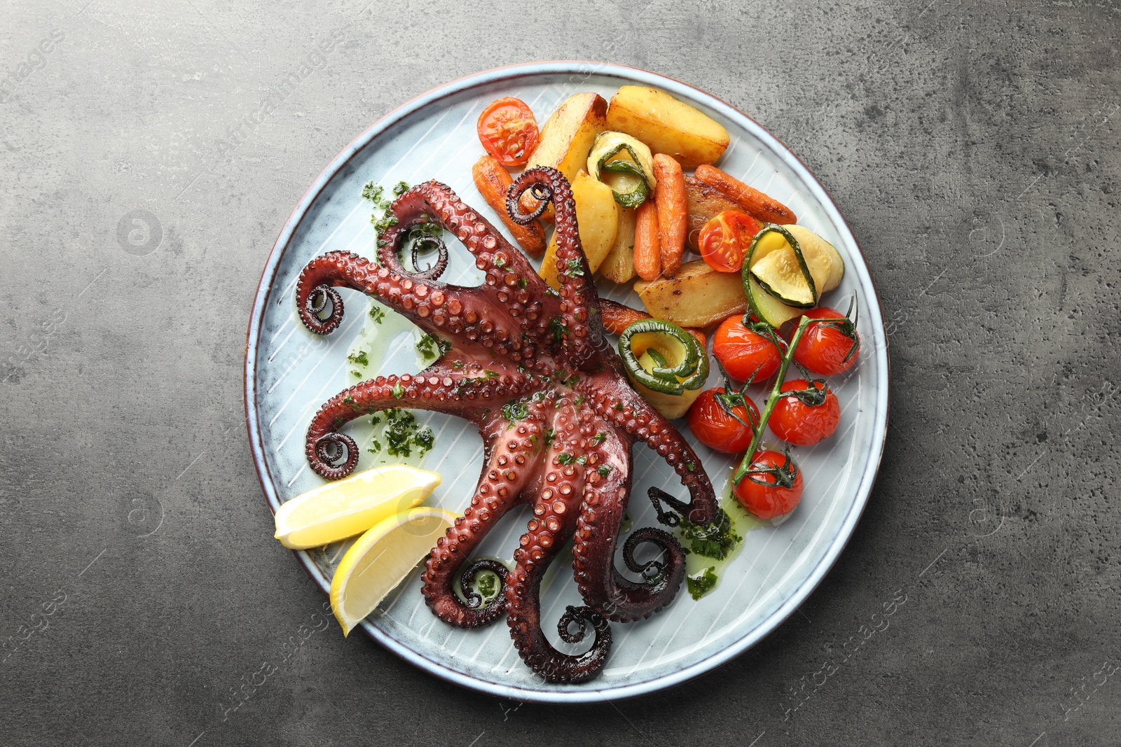 Photo of Fried octopus with herb sauce, lemon and vegetables on grey textured table, top view