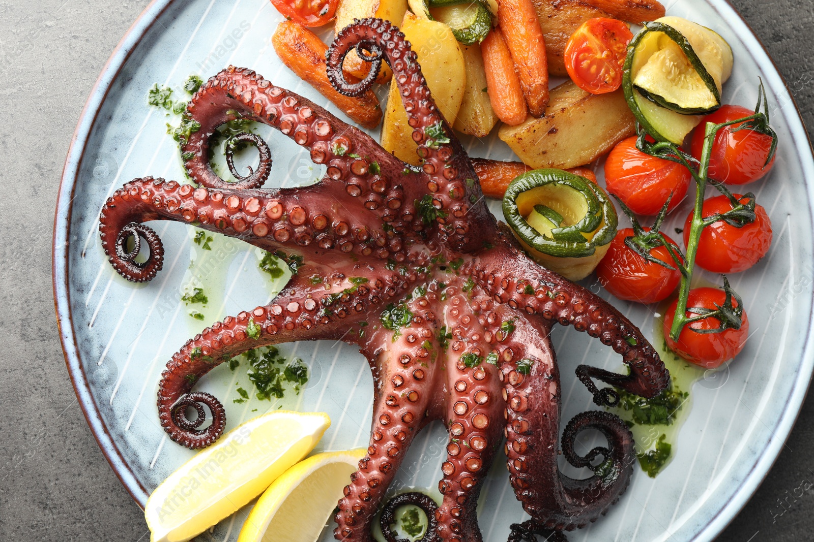 Photo of Fried octopus with herb sauce, lemon and vegetables on grey textured table, top view