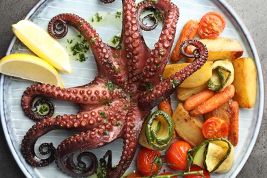 Photo of Fried octopus with herb sauce, lemon and vegetables on grey textured table, top view