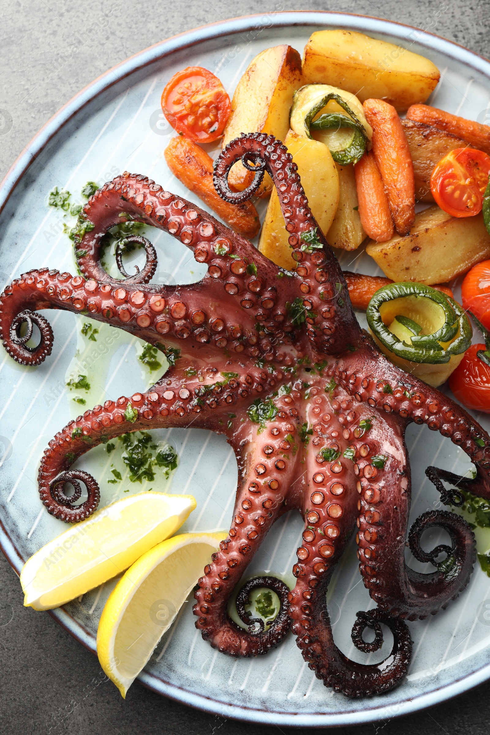 Photo of Fried octopus with herb sauce, lemon and vegetables on grey textured table, top view