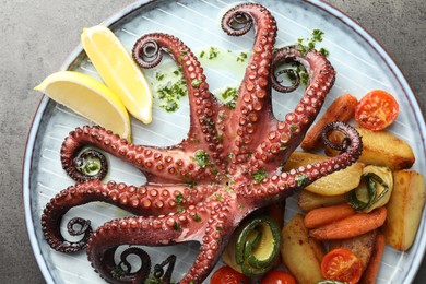 Photo of Fried octopus with herb sauce, lemon and vegetables on grey textured table, top view