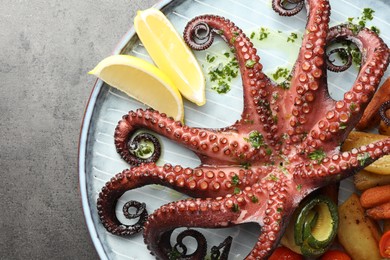 Photo of Fried octopus with herb sauce, lemon and vegetables on grey textured table, top view