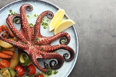 Photo of Fried octopus with herb sauce, lemon and vegetables on grey textured table, top view. Space for text