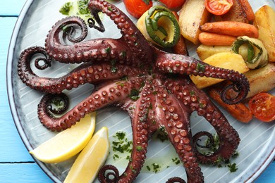 Photo of Fried octopus with herb sauce, lemon and vegetables on light blue wooden table, top view