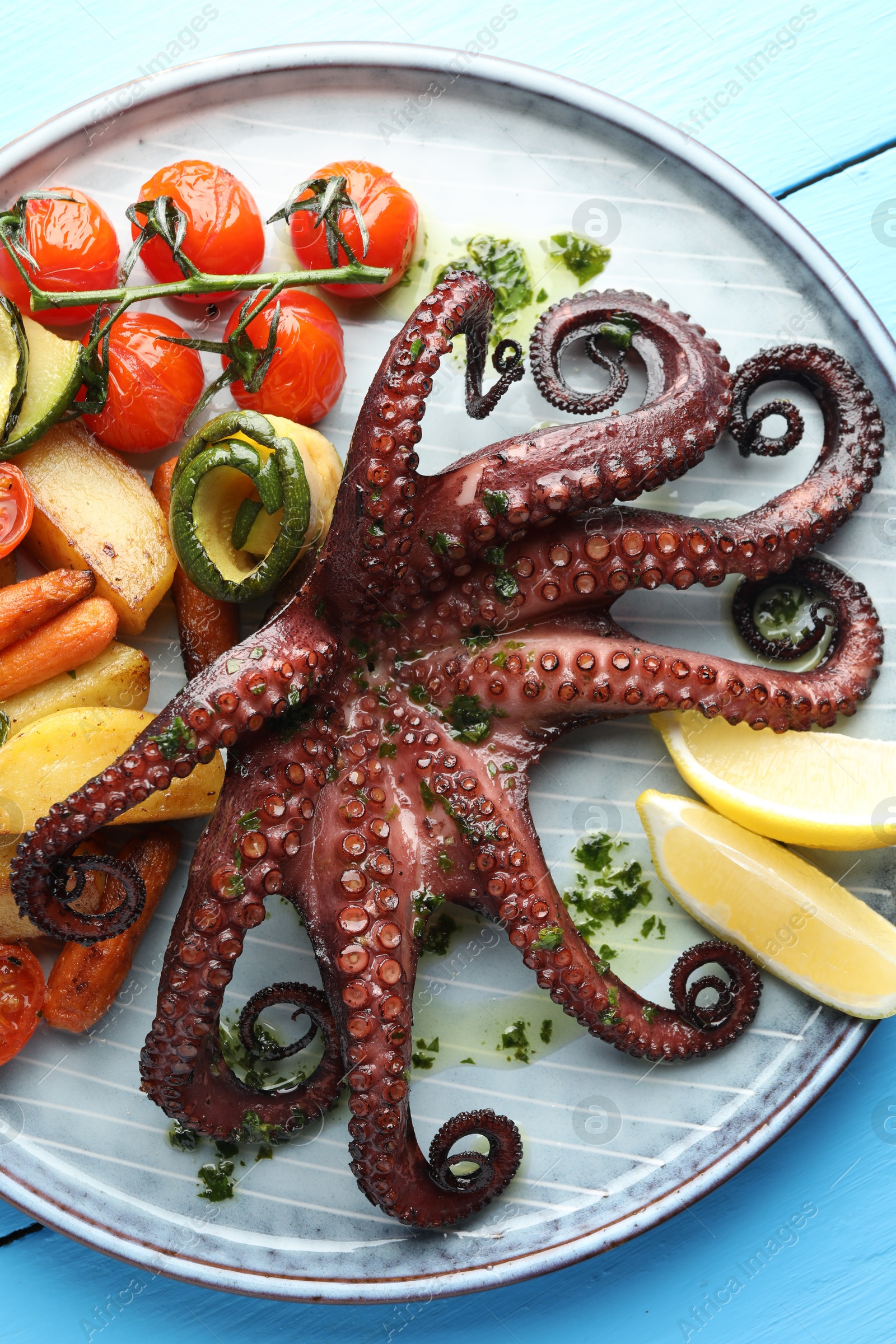 Photo of Fried octopus with herb sauce, lemon and vegetables on light blue wooden table, top view