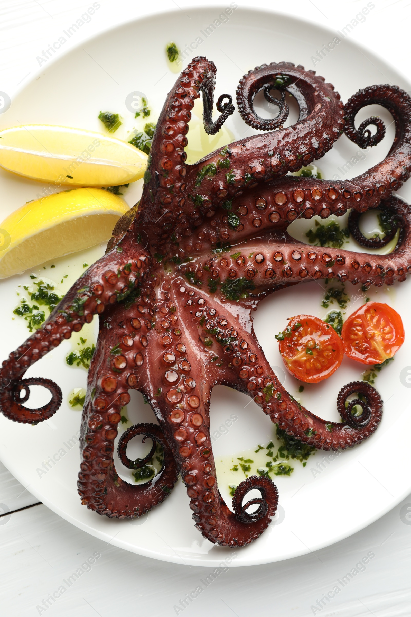 Photo of Fried octopus with herb sauce, lemon and tomatoes on white wooden table, top view