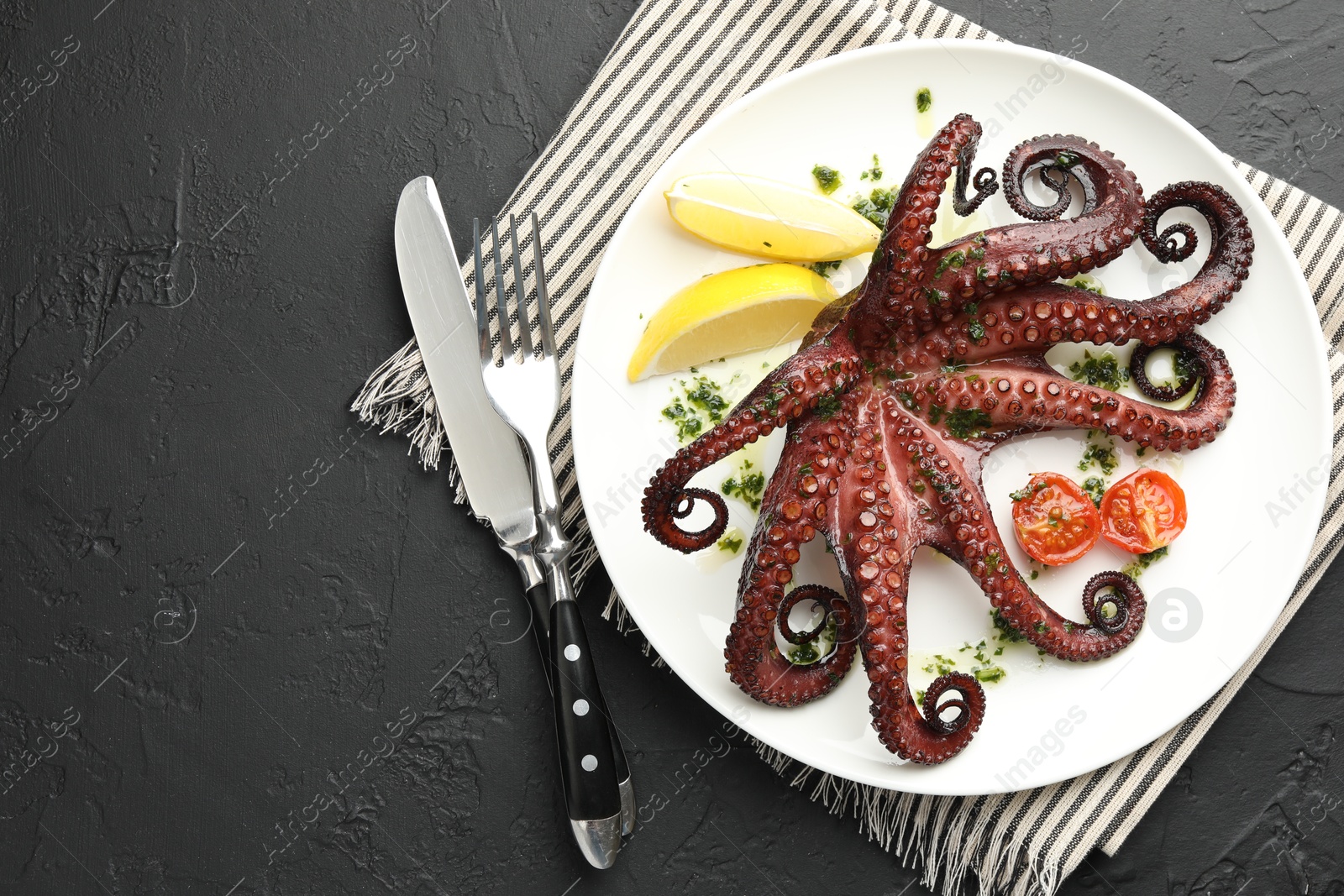 Photo of Fried octopus with herb sauce, lemon and tomatoes served on dark textured table, flat lay. Space for text