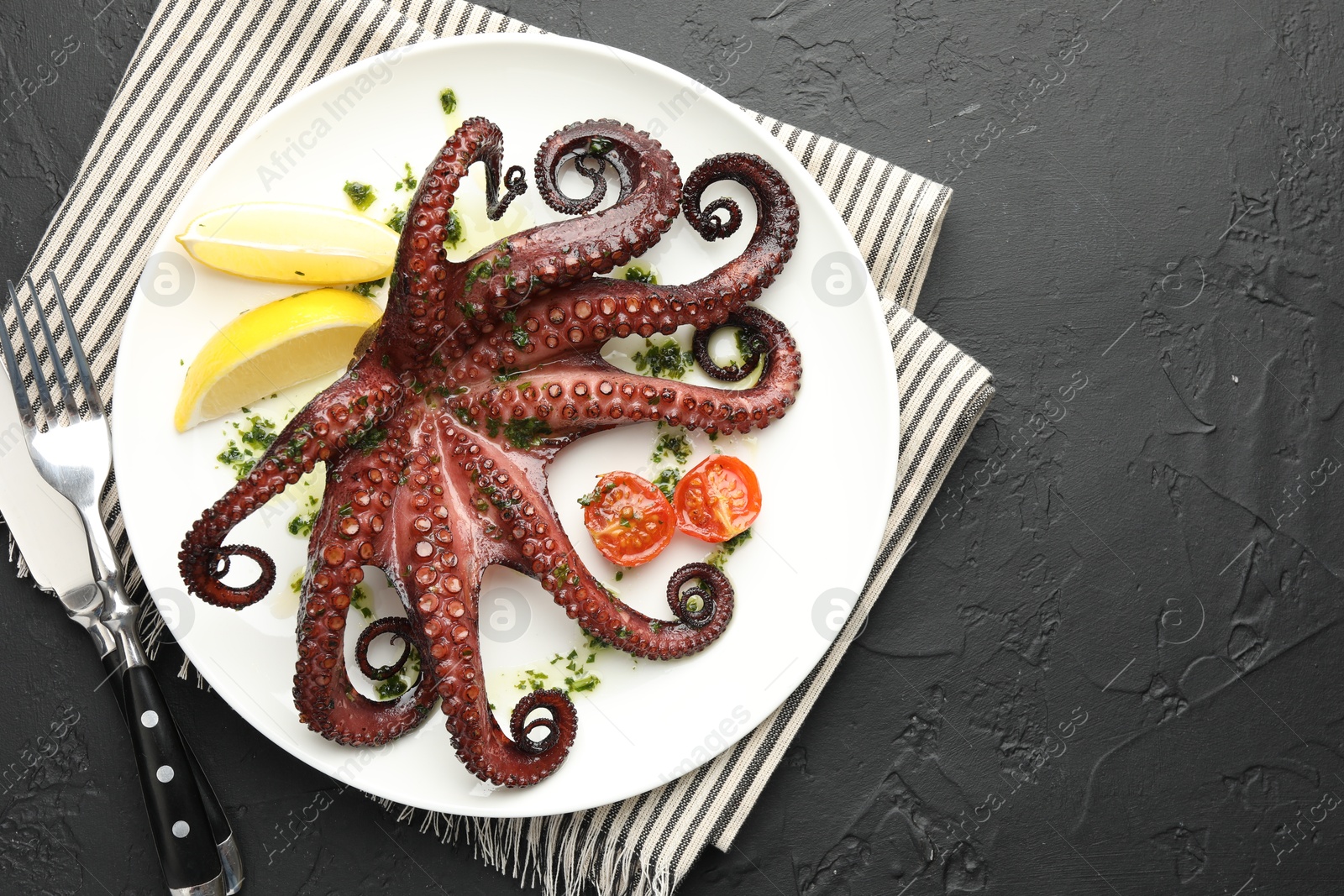 Photo of Fried octopus with herb sauce, lemon and tomatoes served on dark textured table, flat lay. Space for text