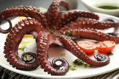 Fried octopus with herb sauce and tomatoes on table, closeup