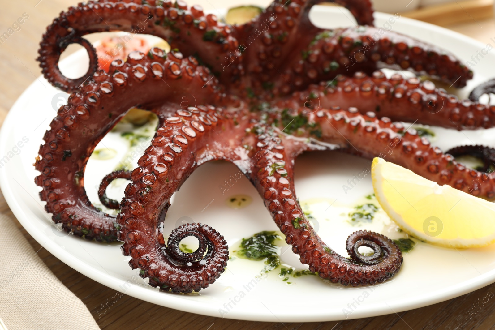 Photo of Fried octopus with herb sauce and lemon on wooden table, closeup