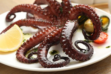 Photo of Fried octopus with herb sauce, lemon and vegetables on wooden table, closeup