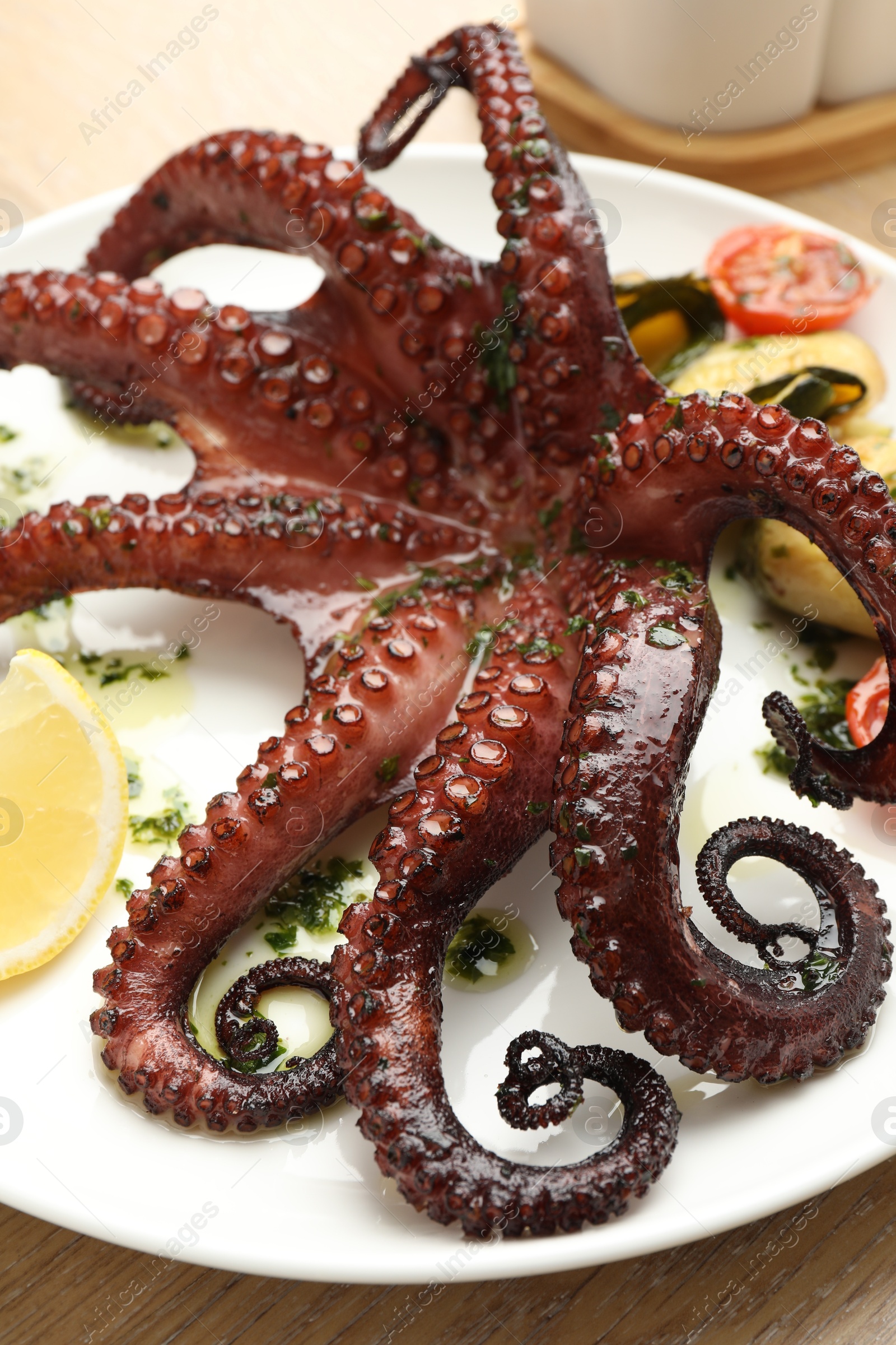 Photo of Fried octopus with herb sauce, lemon and vegetables on wooden table, closeup