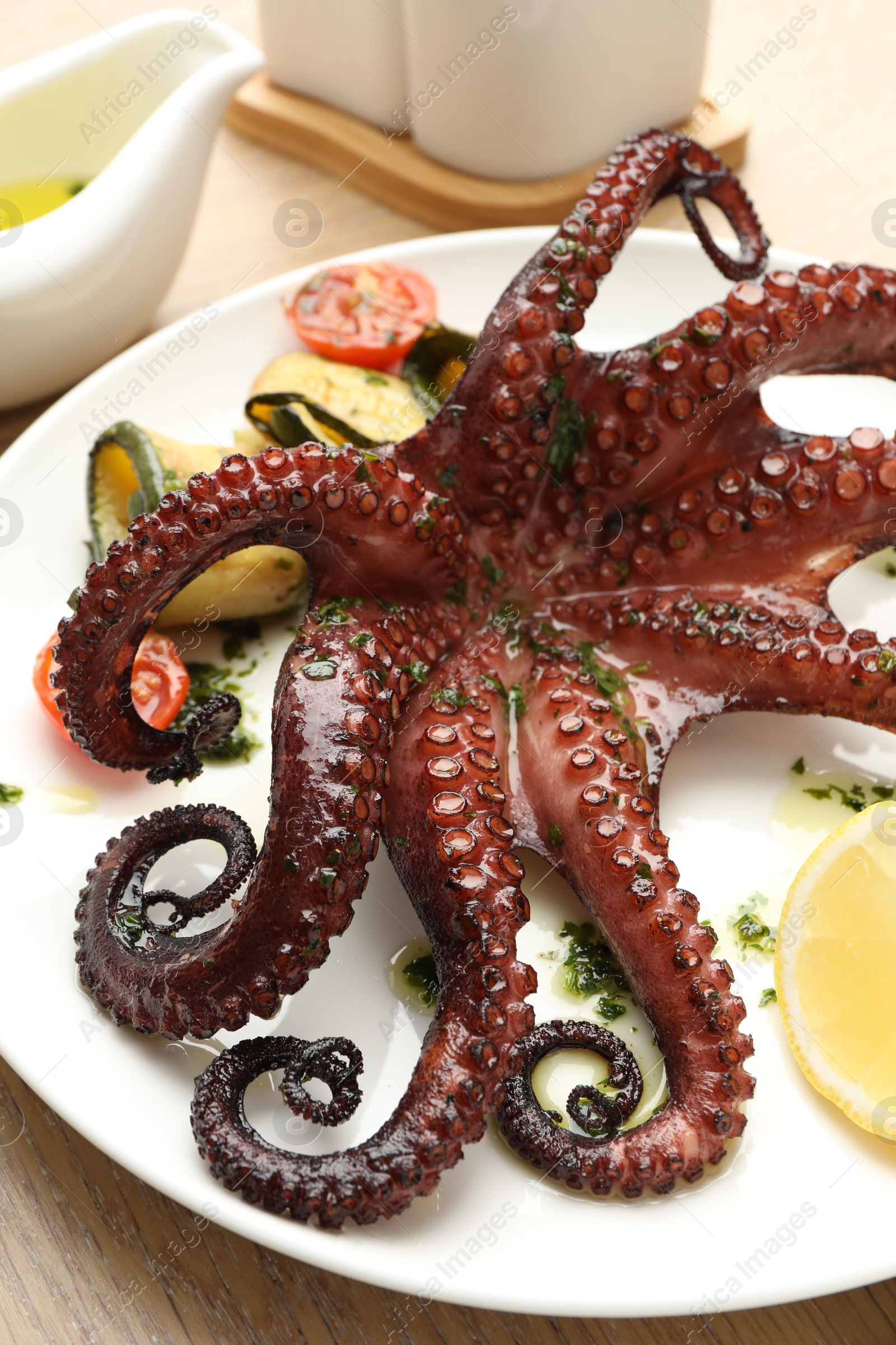 Photo of Fried octopus with herb sauce, lemon and vegetables on wooden table, closeup