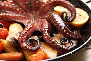 Photo of Fried octopus with lemon and vegetables in pan on wooden table, closeup