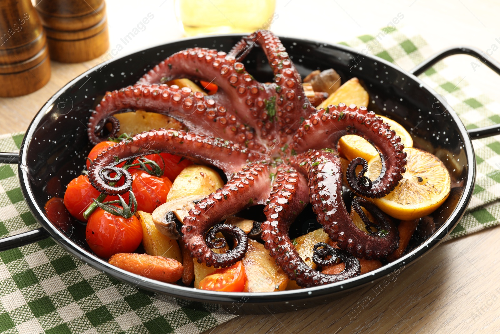 Photo of Fried octopus with lemon and vegetables in pan on wooden table, closeup