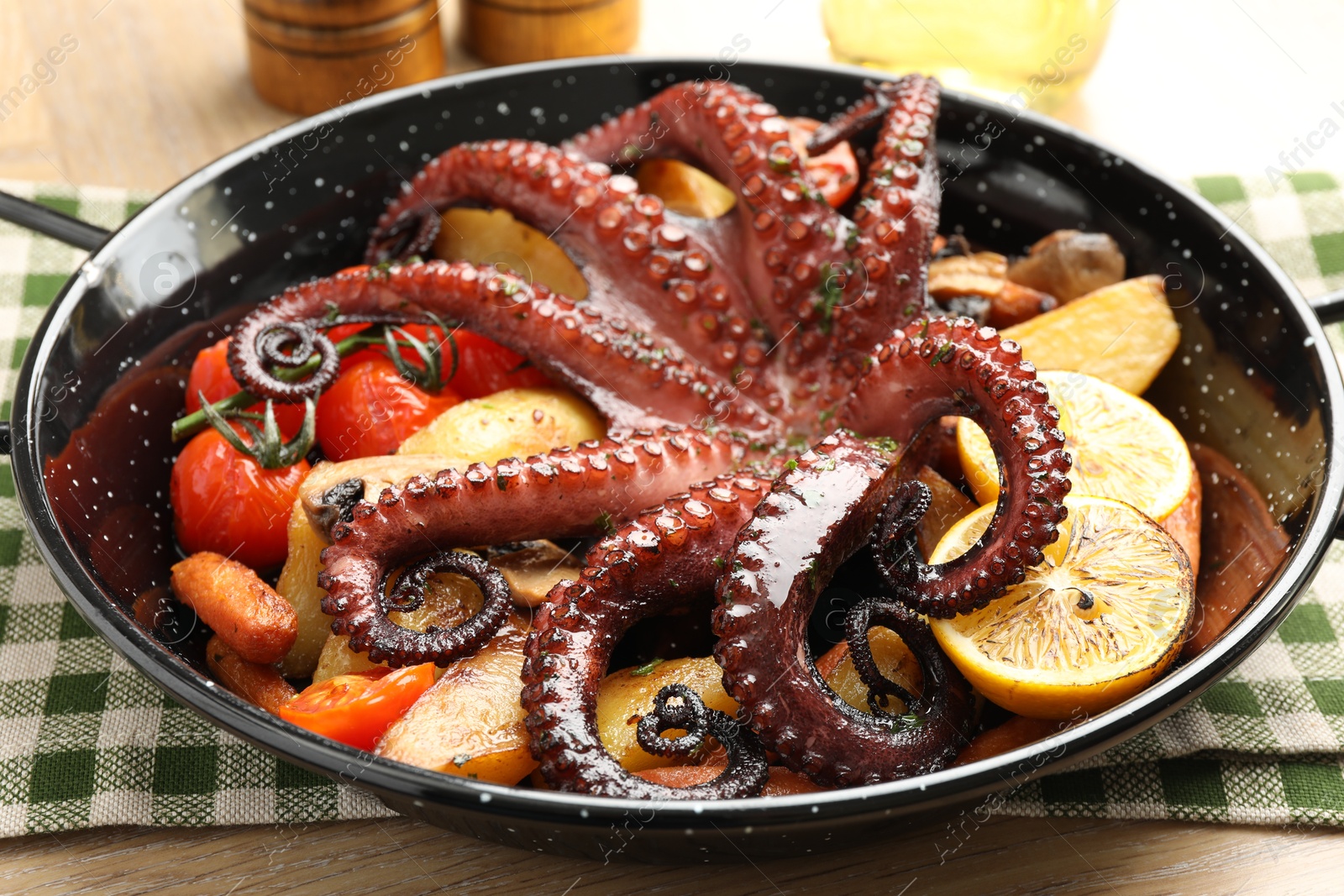 Photo of Fried octopus with lemon and vegetables in pan on wooden table, closeup