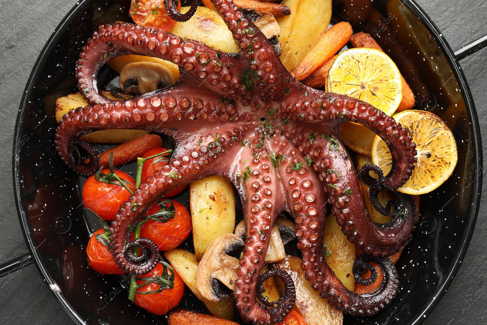 Photo of Fried octopus with lemon, mushrooms and vegetables on grey textured table, top view