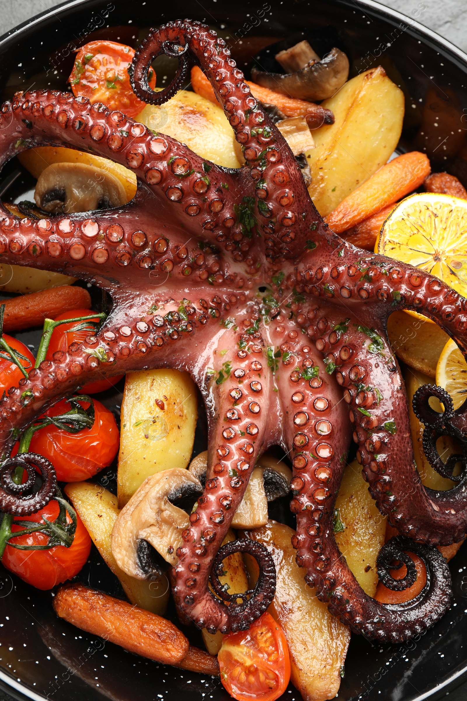 Photo of Fried octopus with lemon, mushrooms and vegetables in pan, above view