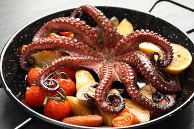 Photo of Fried octopus with lemon, mushroom and vegetables on grey table, closeup