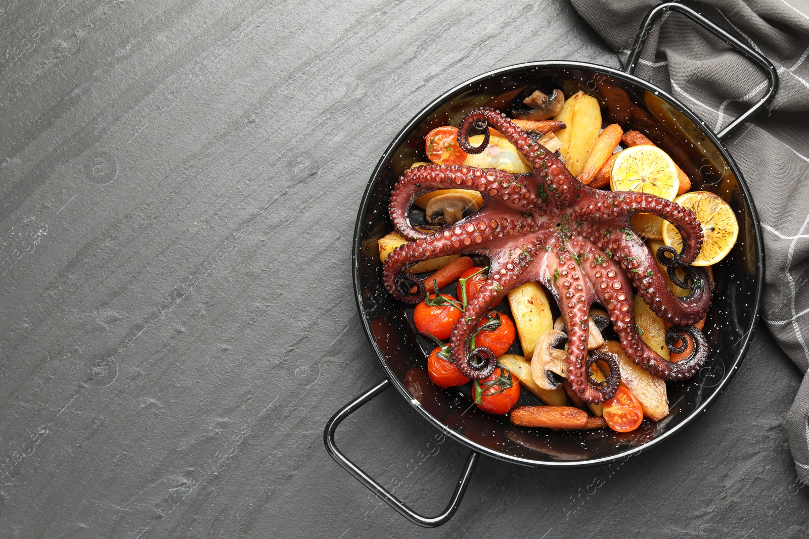 Photo of Fried octopus with mushrooms, lemon and vegetables on grey textured table, top view. Space for text