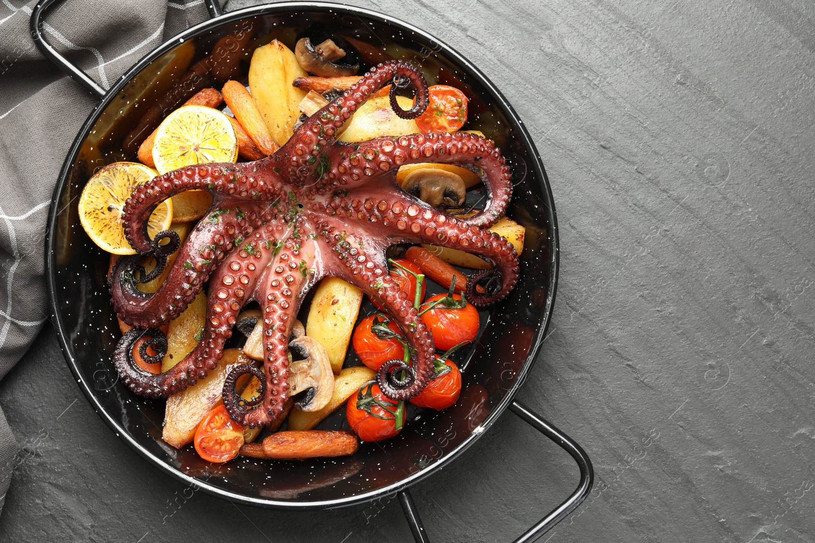 Photo of Fried octopus with mushrooms, lemon and vegetables on grey textured table, top view. Space for text