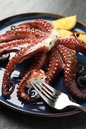 Photo of Fried octopus with herb sauce, lemon and fork on grey table, closeup