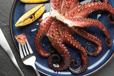 Photo of Fried octopus with herb sauce, lemon and cutlery on grey textured table, flat lay