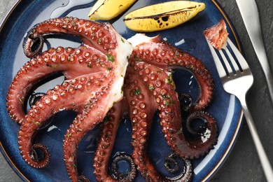 Photo of Fried octopus with herb sauce, lemon and cutlery on grey textured table, flat lay