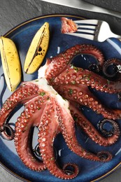 Photo of Fried octopus with herb sauce, lemon and cutlery on grey textured table, flat lay