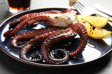 Photo of Fried octopus with herb sauce and lemon on grey table, closeup