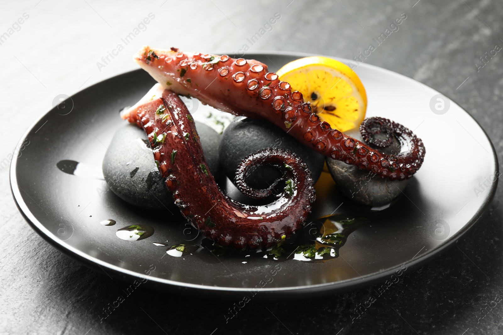 Photo of Fried octopus with herb sauce and lemon served on grey textured table, closeup