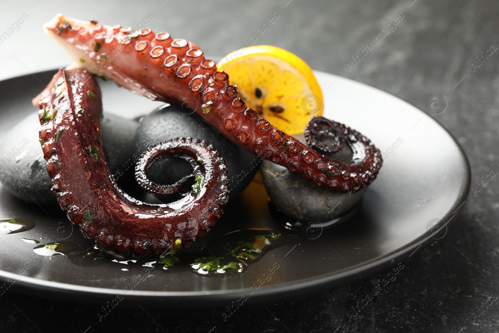 Photo of Fried octopus with herb sauce and lemon served on grey textured table, closeup